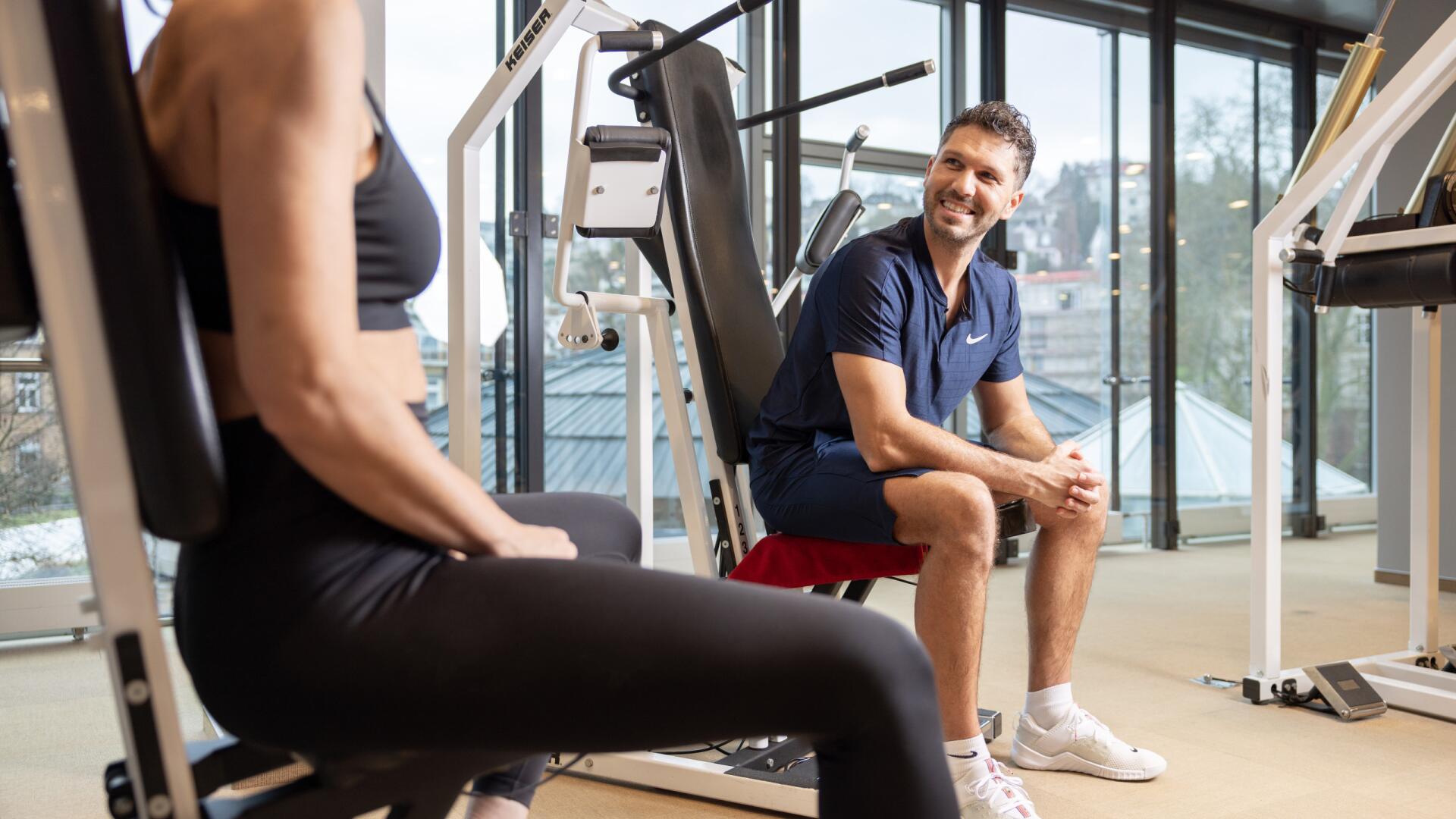 Trainer im ArenaVita Fitnessclub in Baden-Baden betreut eine Frau beim Training an den Geräten.