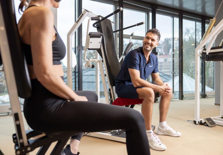 Trainer im ArenaVita Fitnessclub in Baden-Baden betreut eine Frau beim Training an den Geräten.