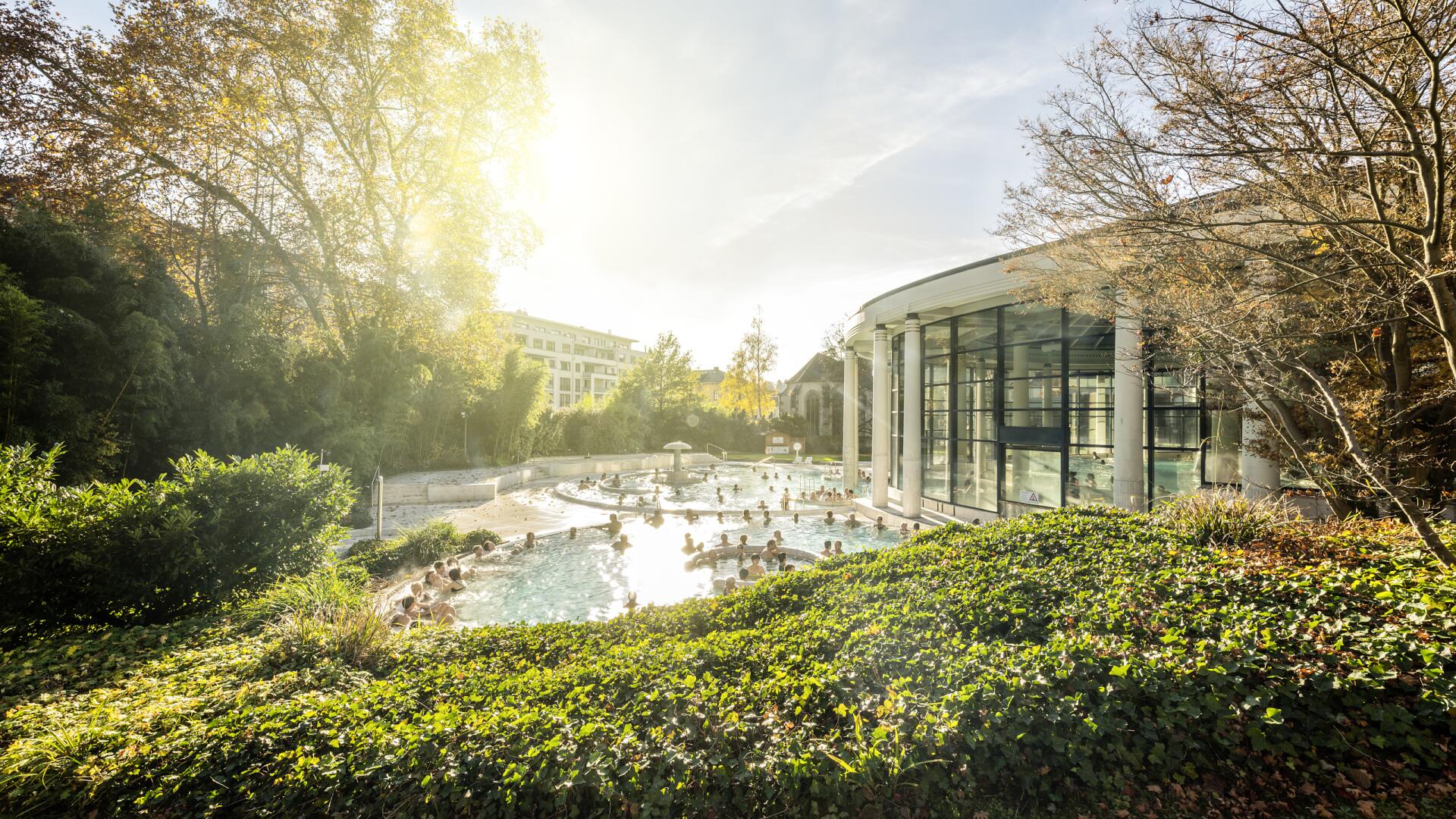 Caracalla Therme Baden-Baden mit dampfendem Außenbecken, Badegästen und moderner Glasarchitektur.
