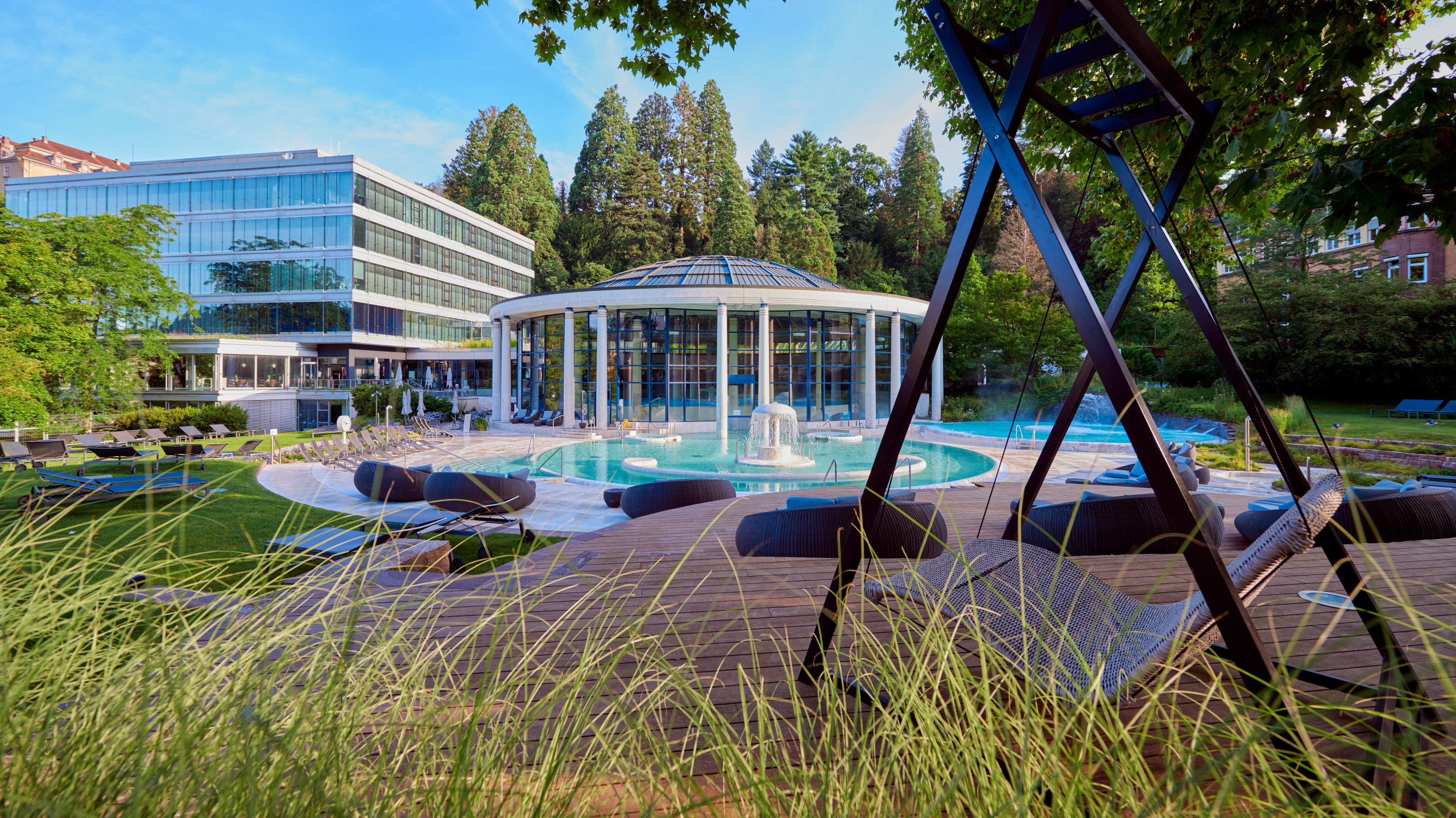 Caracalla Therme Baden-Baden mit Glasrotunde und Außenbecken, fotografiert durch Gräser im Vordergrund.